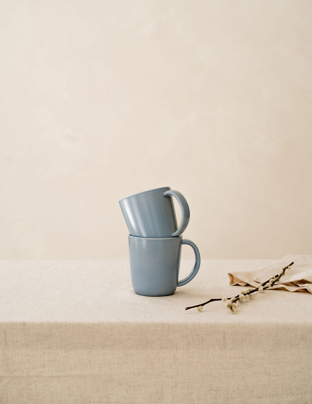 Stacked Wave blue ceramic mugs by Hamkke Home on a neutral linen table.