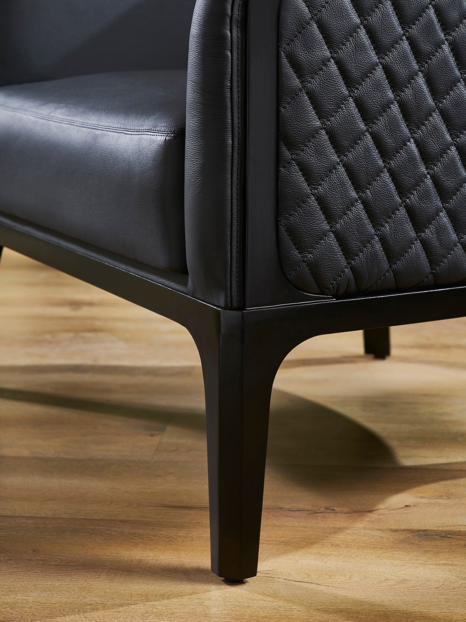FN-5205-343329_7|Detail of modern black leather armchair's dark wooden tapered legs, highlighting robust construction and elegant contemporary design.