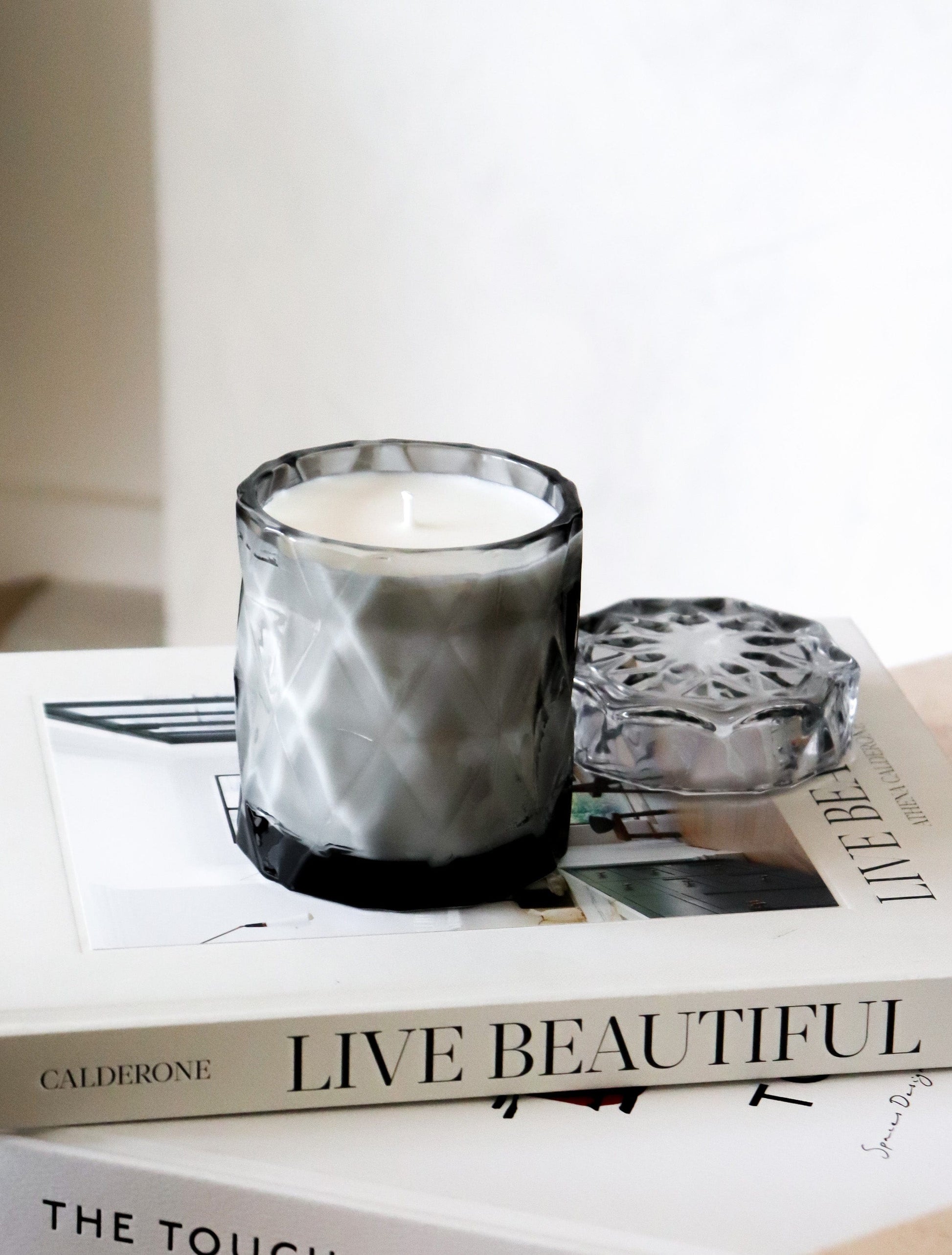 coconut wax candles in a gray glass jar with lid on stacked coffee table books