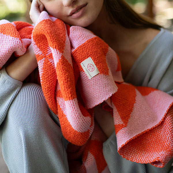 Lady holding a soft neon orange and pink knitted cotton blanket against her face. 