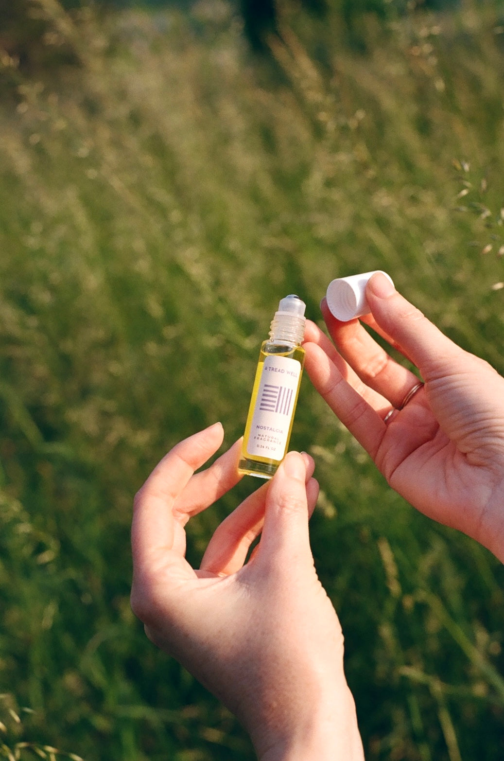 Two small bottles of fragrance held in hands against a blurred grassy background