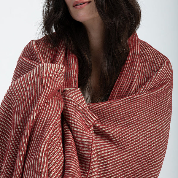 Woman with shoulder length hair wearing a red and white ribbed and textured comfortable throw blanket.