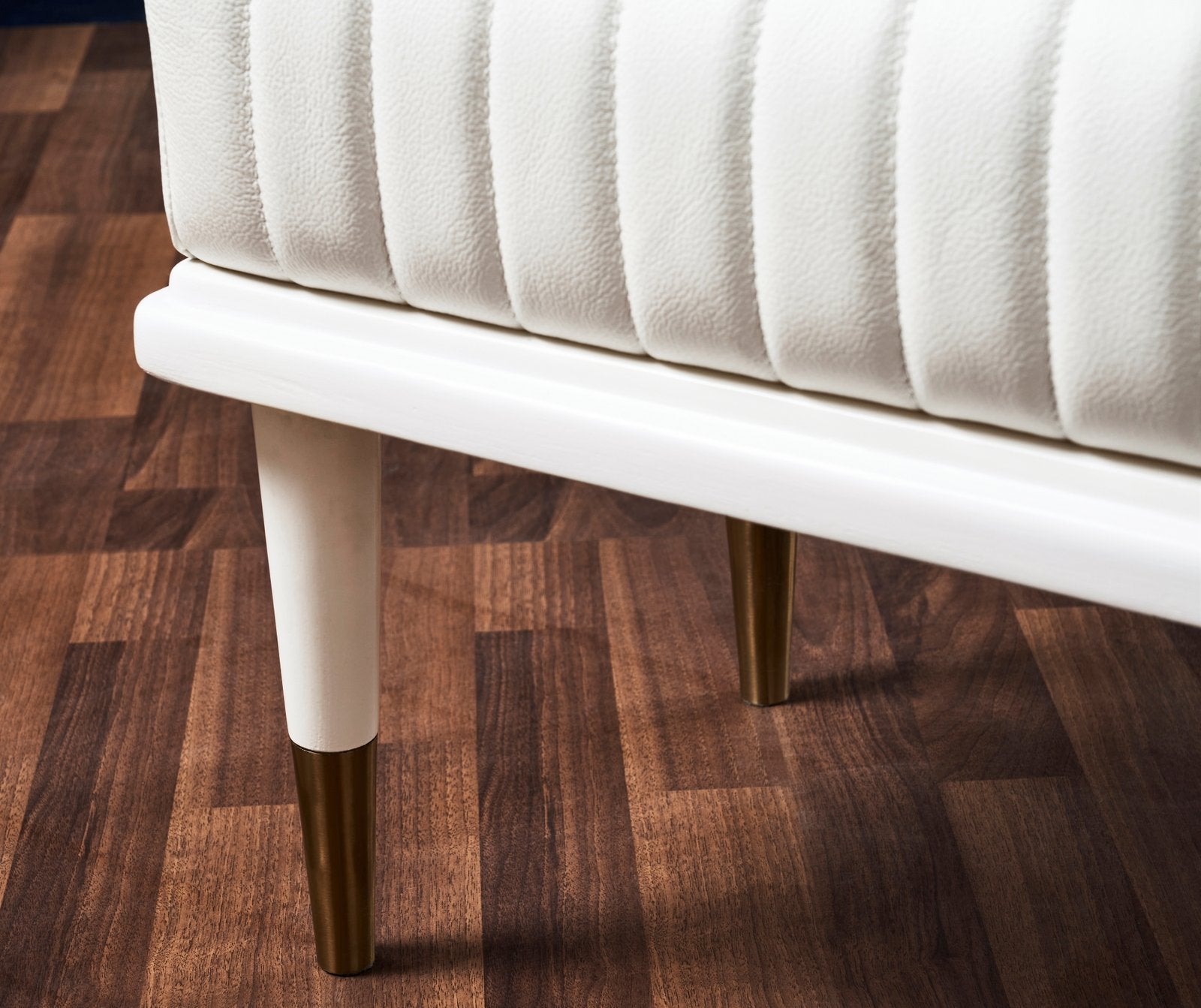FN-5203-601618_7|Close-up of white leather bench legs with gold tips on dark wood floor, showcasing modern luxury furniture detail.