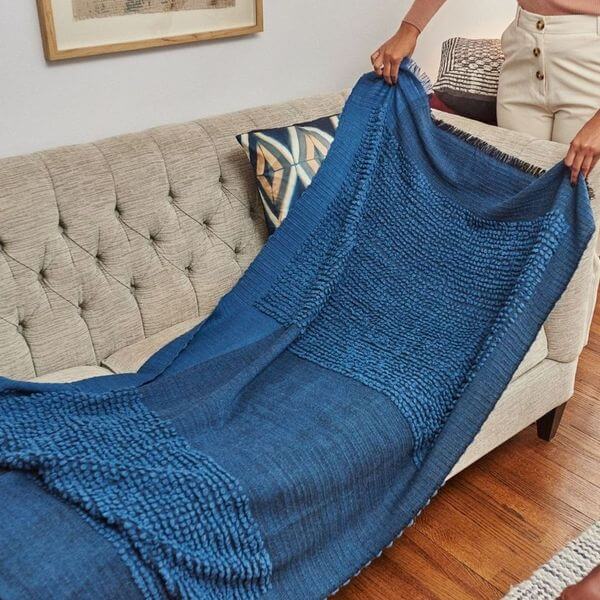 Macaroon Midnight Dark Blue Textured Merino Handloom Throw elegantly draped over a beige sofa.