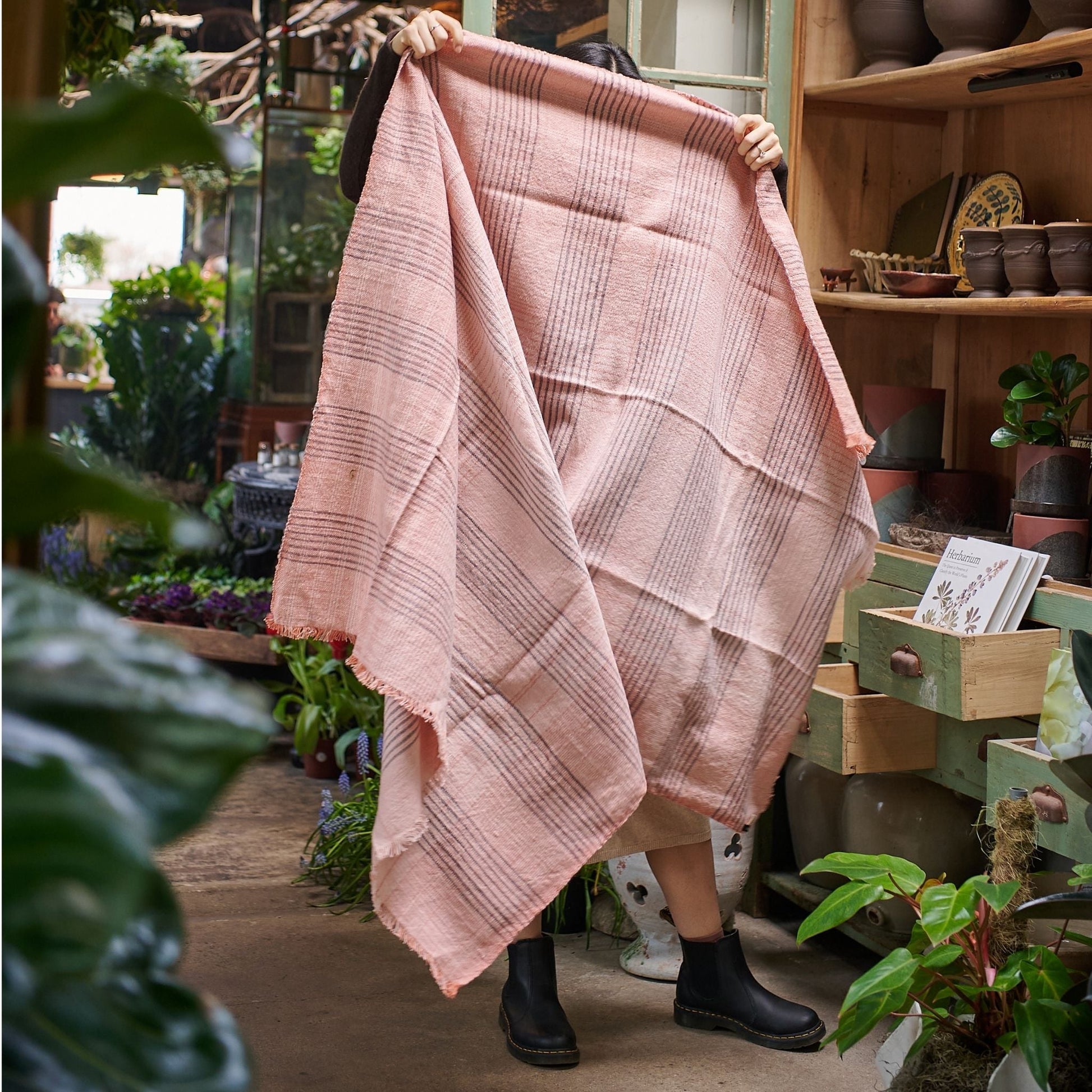Silica Rose In Shades of Salmon Pink Gray Stripes Pattern Soft Handwoven Merino Throw displayed in a vibrant plant-filled setting.