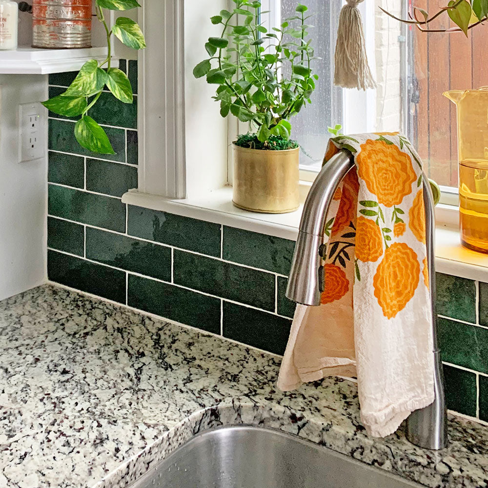 The Neighborgoods Marigolds dish towel hangs over a kitchen sink faucet.