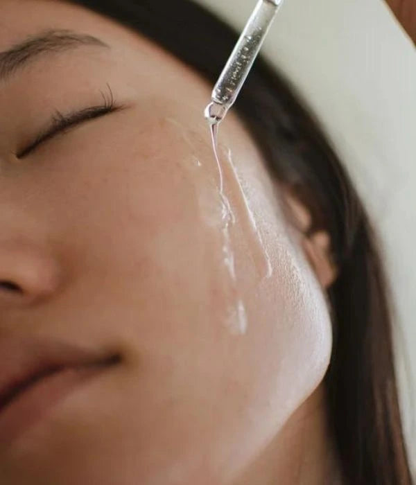 Close-up of a woman's face with a dropper applying a serum to her skin.
