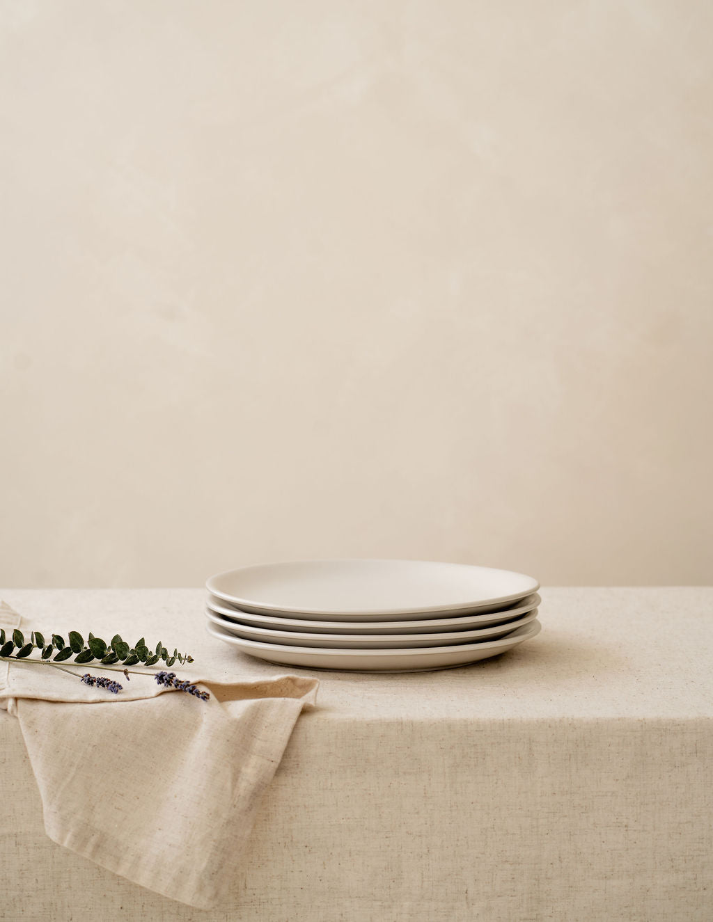 Bone ibory non-toxic ceramic dinner plates from Hamkke Home stacked on a neutral linen tablecloth with floral accent.