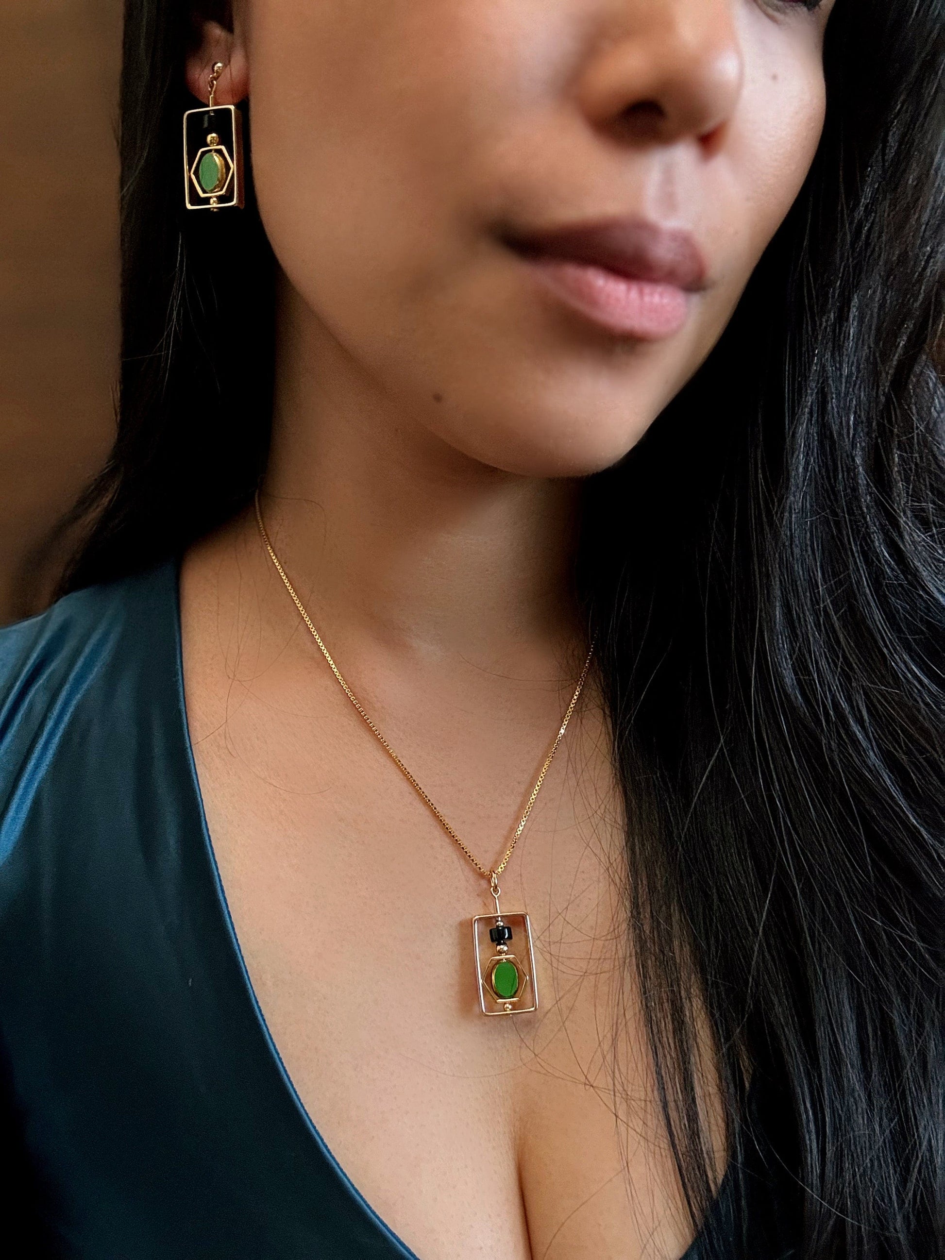 Close-up of a person wearing a gold necklace with a green gemstone pendant and matching earrings.