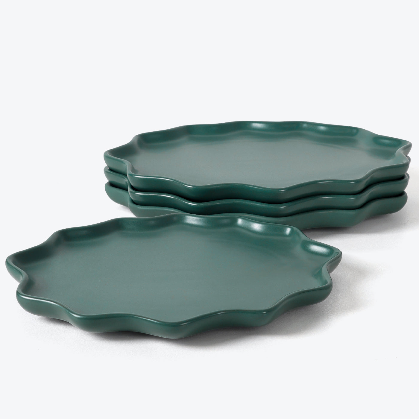 Set of four green ceramic trays with scalloped edges on a white background