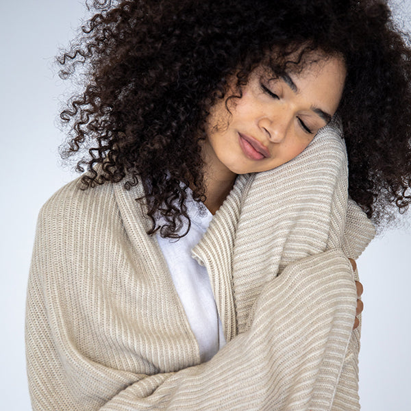 Woman wrapped in a soft beige organic cotton blanket with a neutral background.