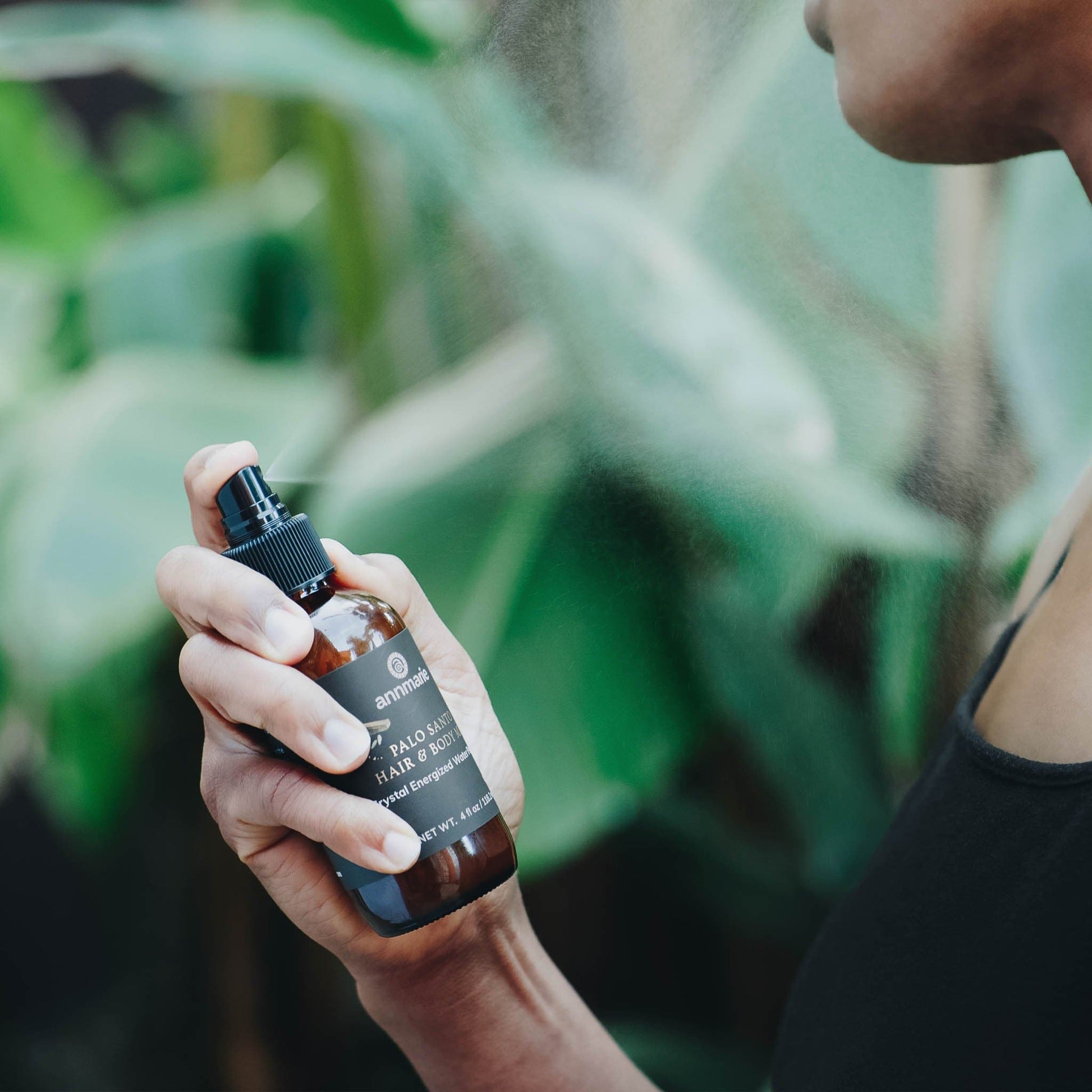 Hand holding a bottle of hair product with a blurred green background