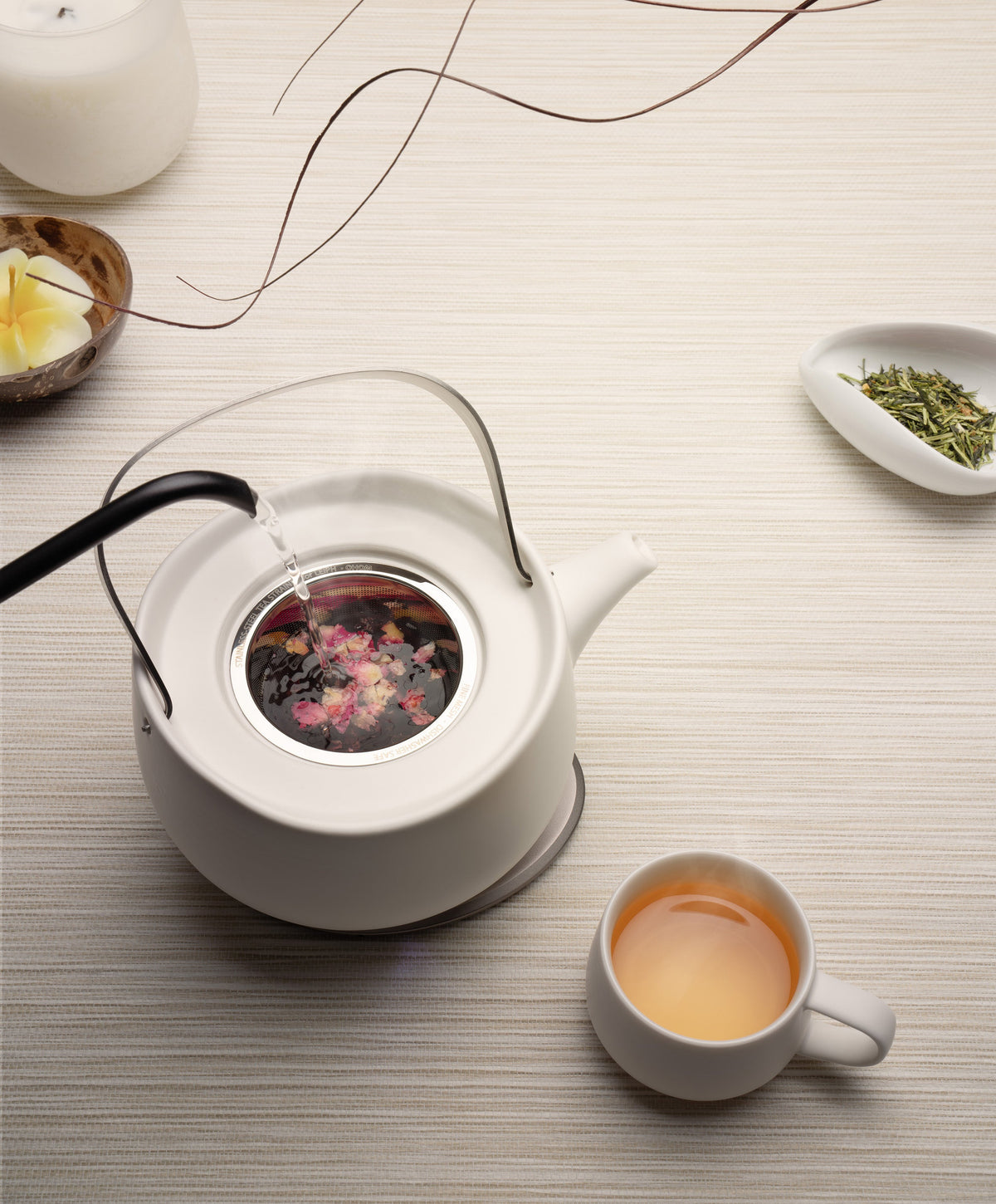 Pouring hot water into Leiph self-heating teapot on OHOM Pad, brewing tea with steam rising beside teacup