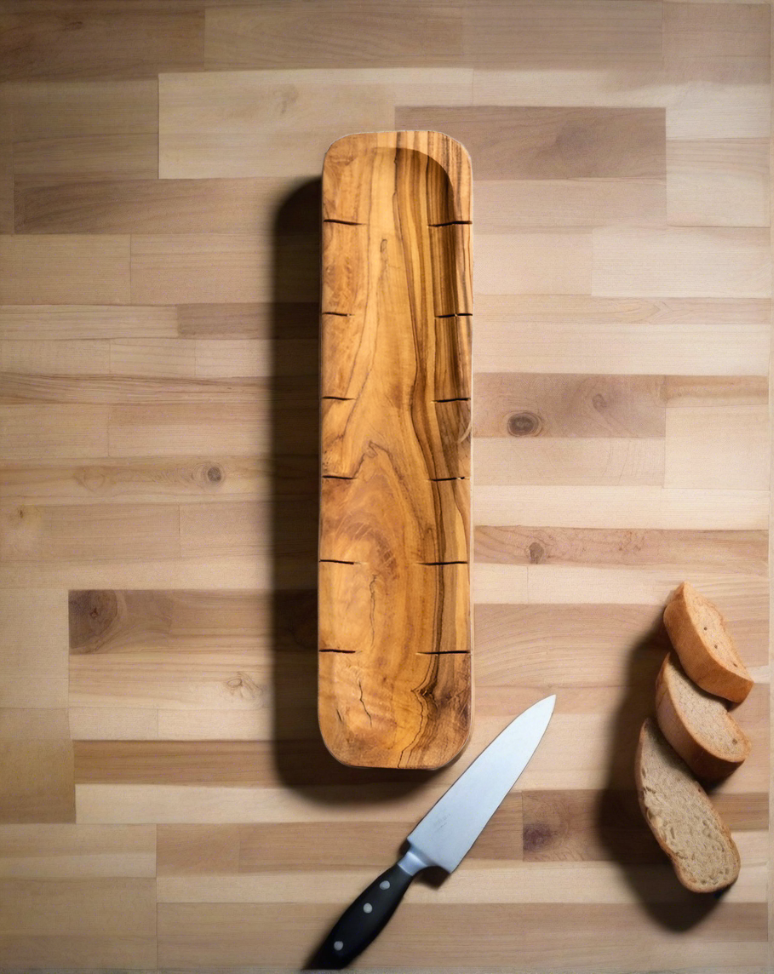 Olive wood bread slicing board laid flat with a knife beside it, and three pieces of bread placed nearby