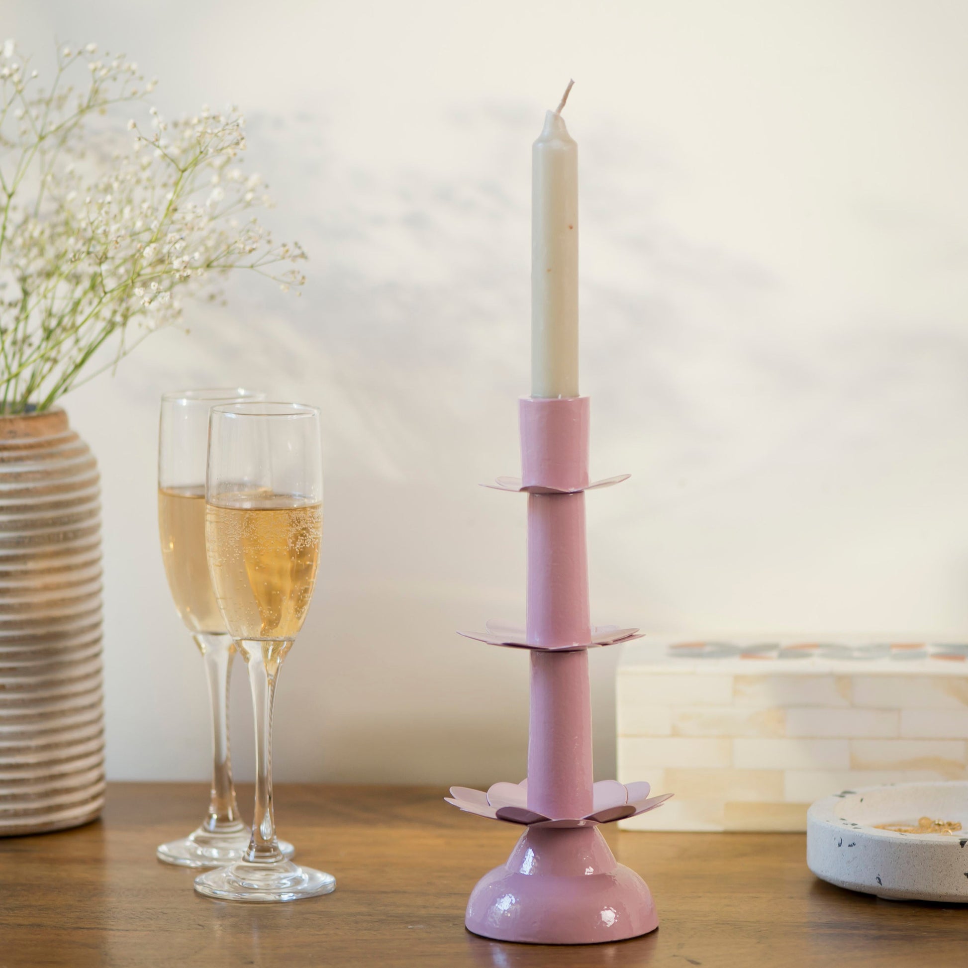 Handcrafted pink lotus candleholder styled on a wooden table alongside two champagne flutes and delicate white flowers.