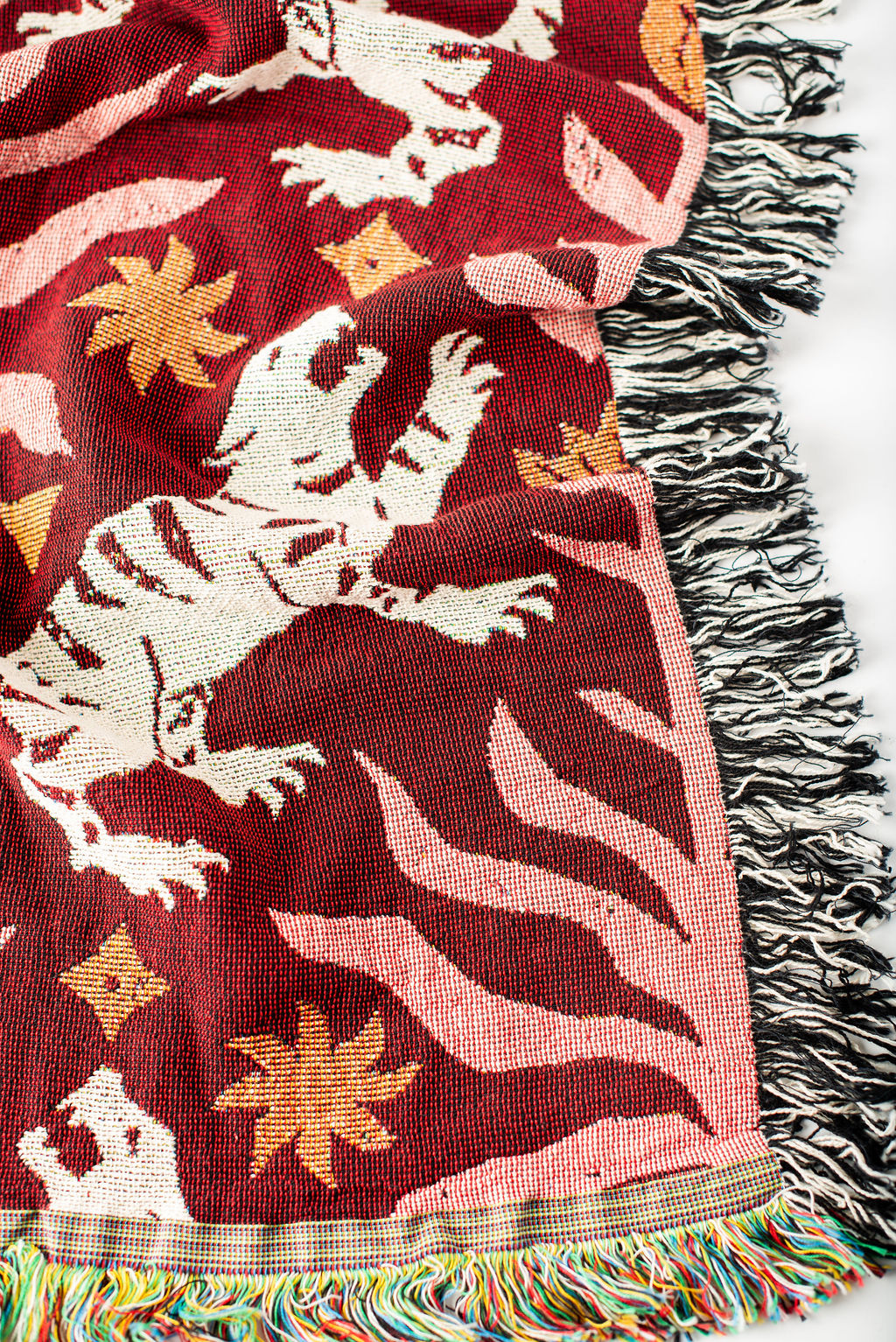 Close-up of Leona Solstice red, coral, cream, and gold tiger folk-art jacquard woven blanket with fringe