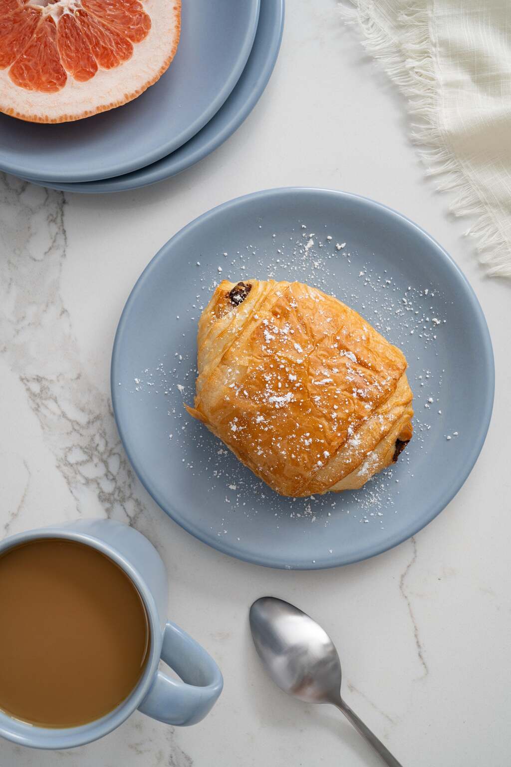Wave blue Petite Plate by Hamkke Home styled with a chocolate croissant, grapefruit, and coffee on a marble surface.