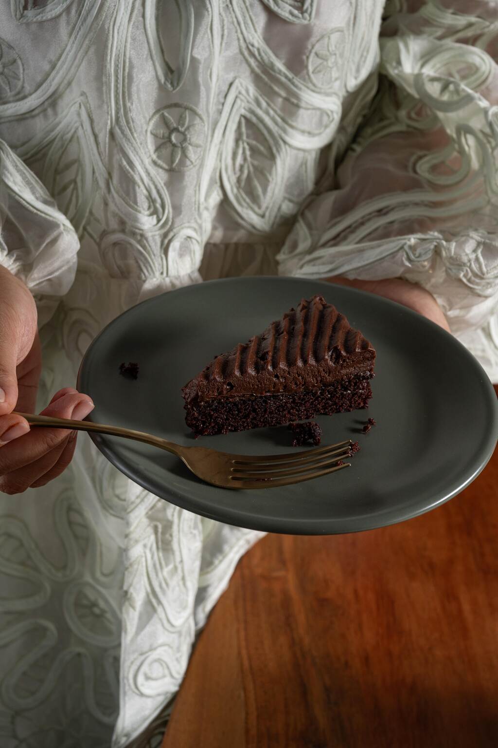 Slice of chocolate cake served on a Moss green ceramic plate from Hamkke Home, held with a brass fork over a wooden table.