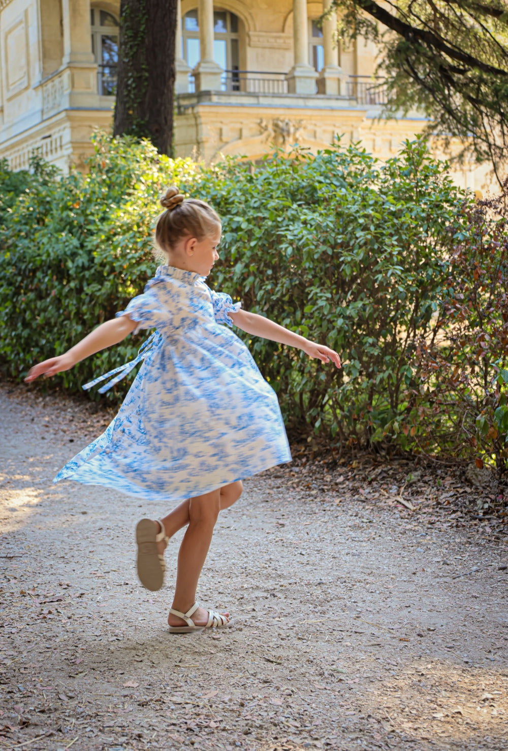 Young girl in a blue floral dress dancing in a park with a classical building in the background