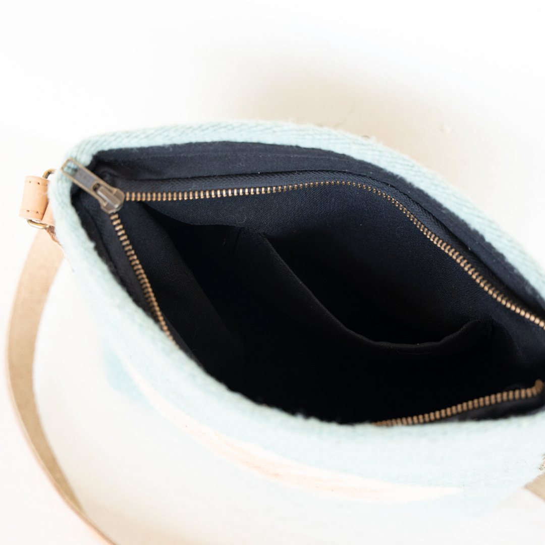 Handwoven crossbody bag with minimalist Zapotec butterfly design in soft blue tones; features adjustable leather strap and two internal pockets for daily essentials