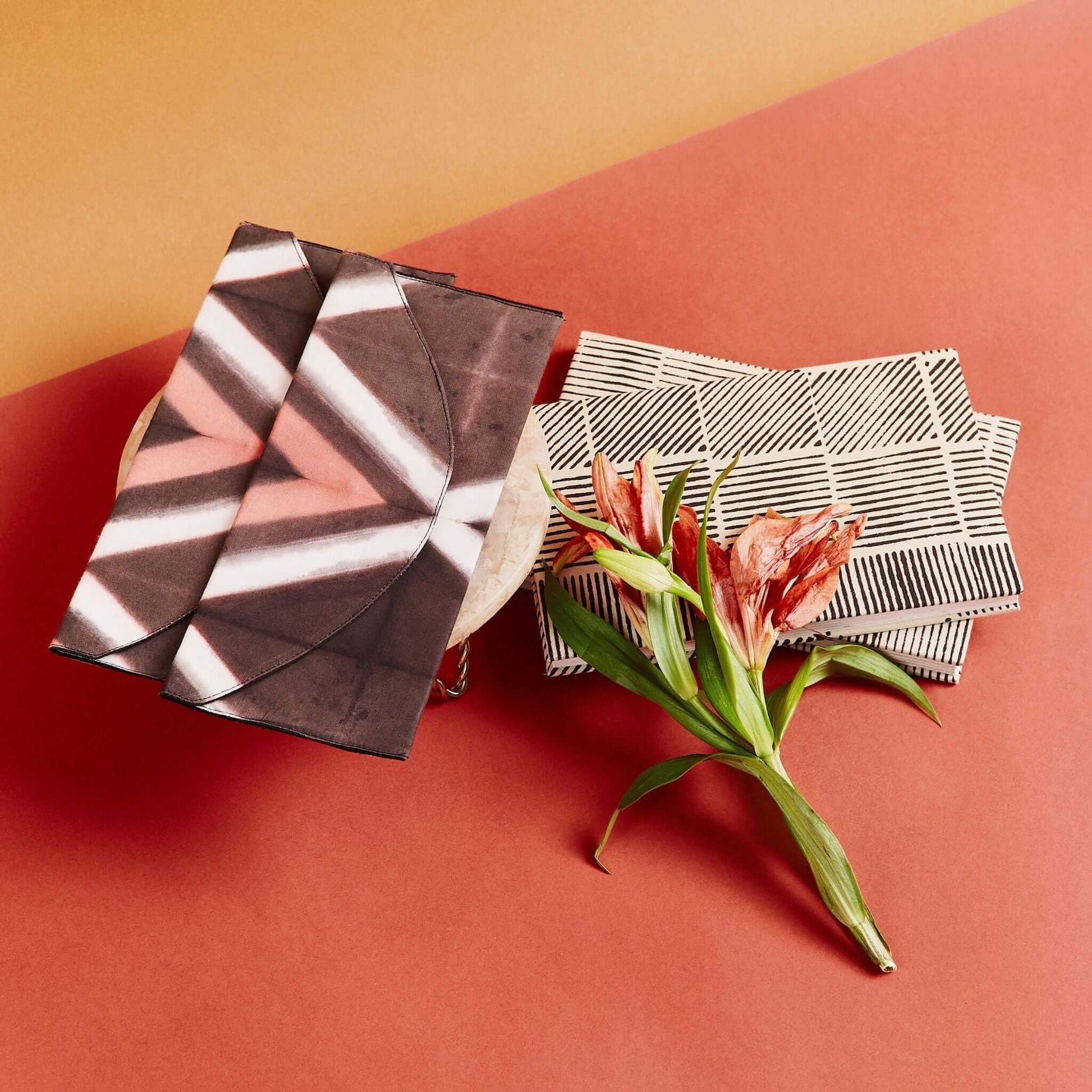 Tisa Artisanal Pouch In Black Pink Triangle Print displayed with geometric patterned pouches and a flower.