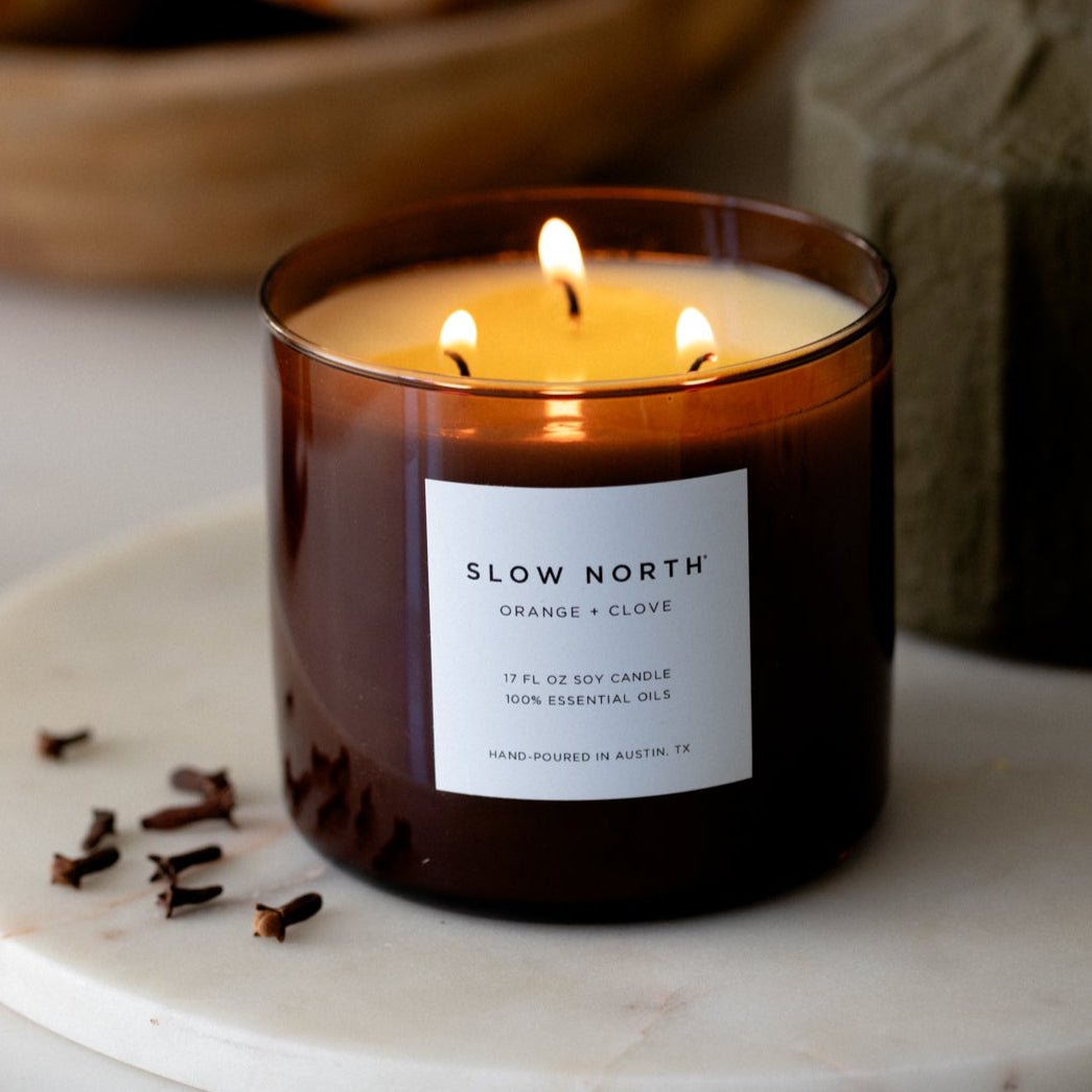 Candle in a glass jar labeled 'Slow North' on a marble surface with decorative elements in the background.