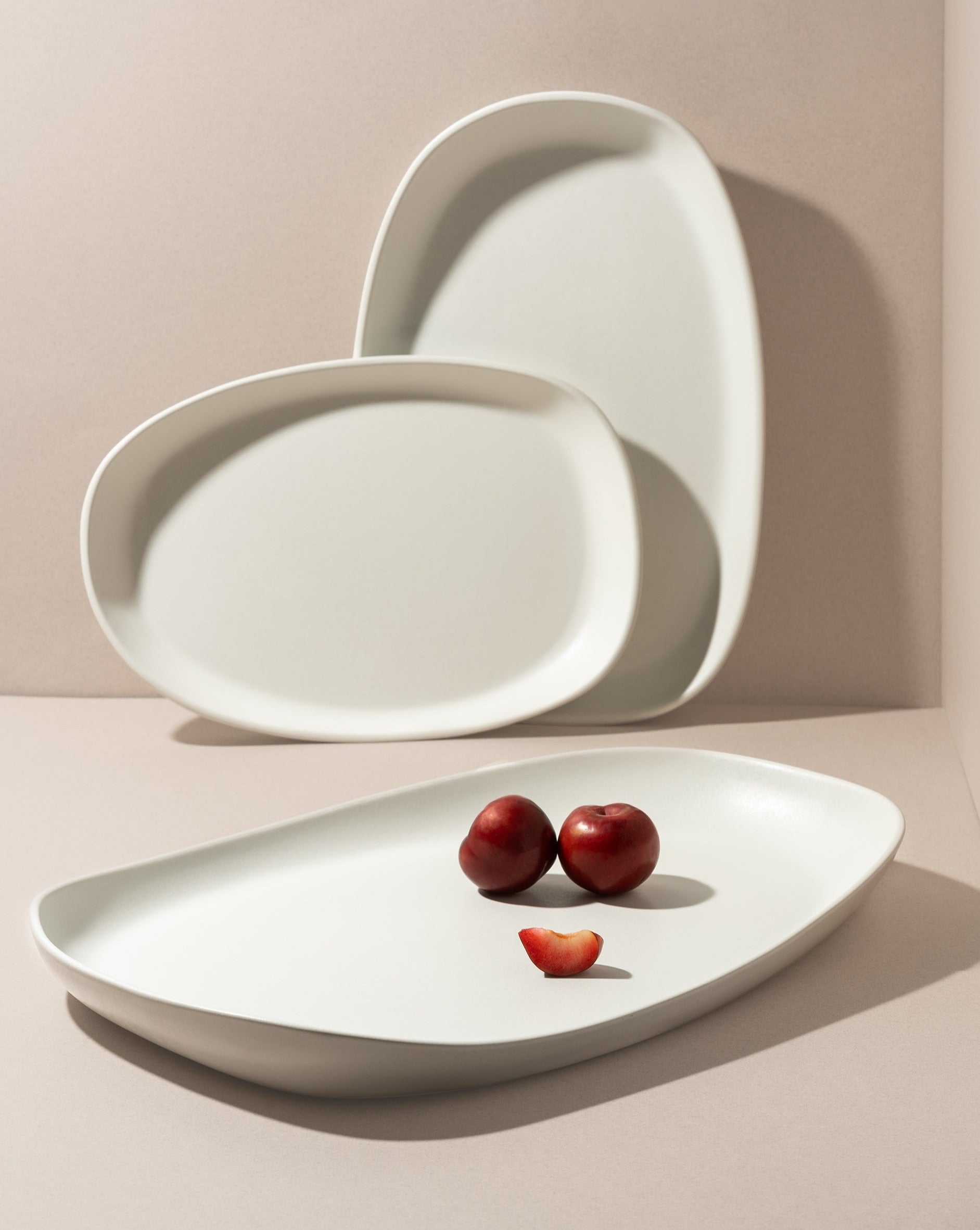 Mini stoneware serving platter with a selection of pastries and blackberries displayed on a kitchen countertop. Two additional serving platters are standing nearby—one in a landscape orientation and the other in a portrait position—showcasing different views of the design.