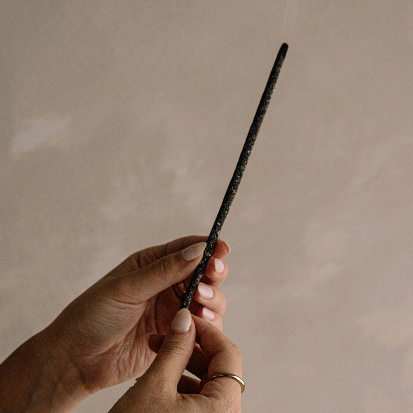 Hand holding smoldering incense stick with gentle smoke rising