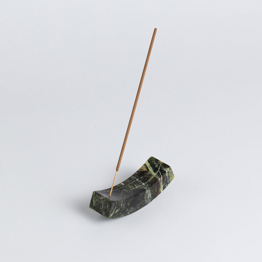 Angled view of the serpentine stone curved incense holder emphasizing its matte finish and heavy materiality on a white background.