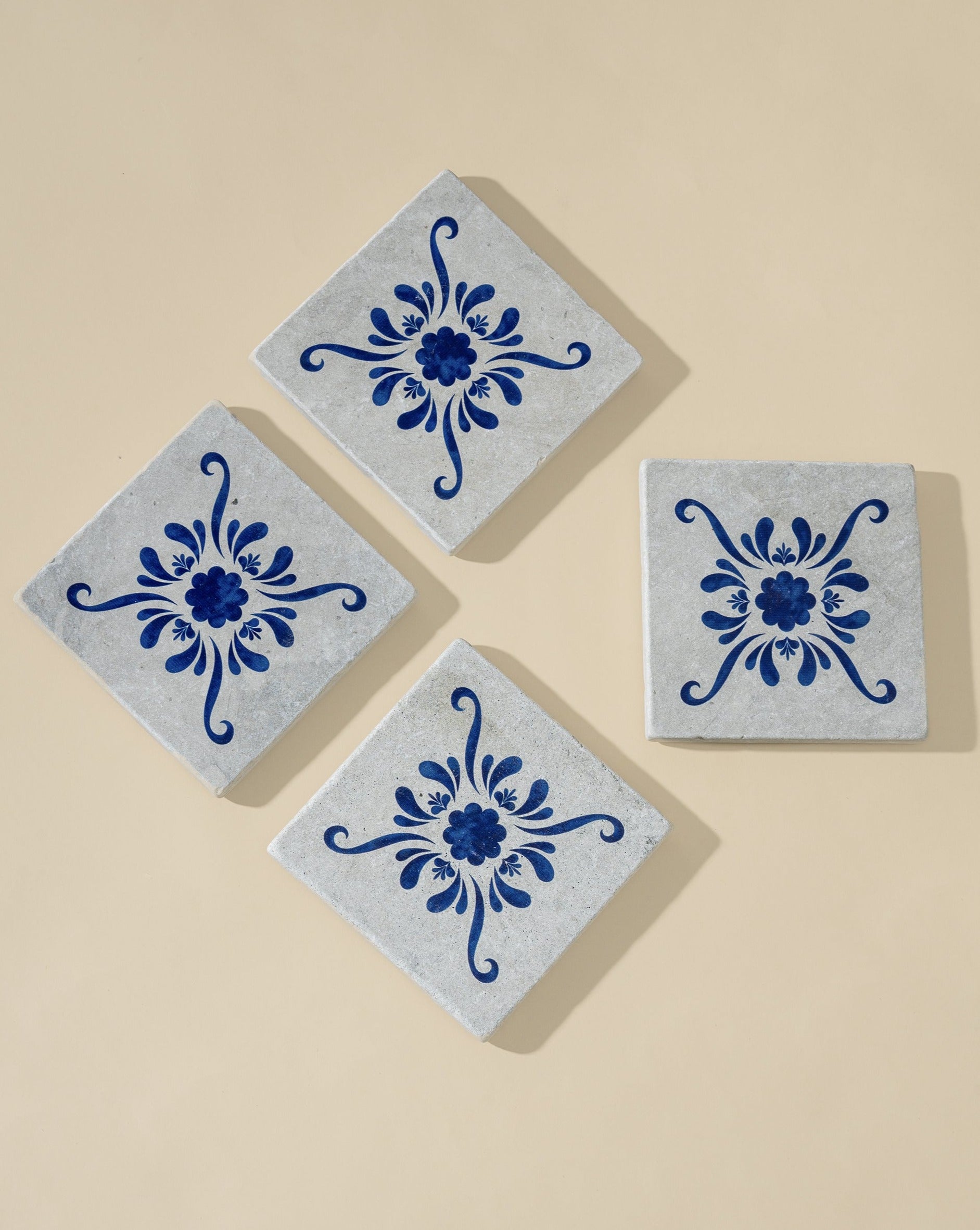 A set of four square white marble coasters with blue floral patterns, evenly arranged on a white background, showcasing their clean design and intricate detailing.