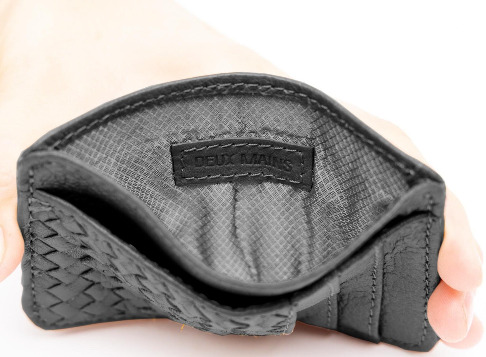 Black leather woven wallet held in a hand with 'DEUX MARS' branding