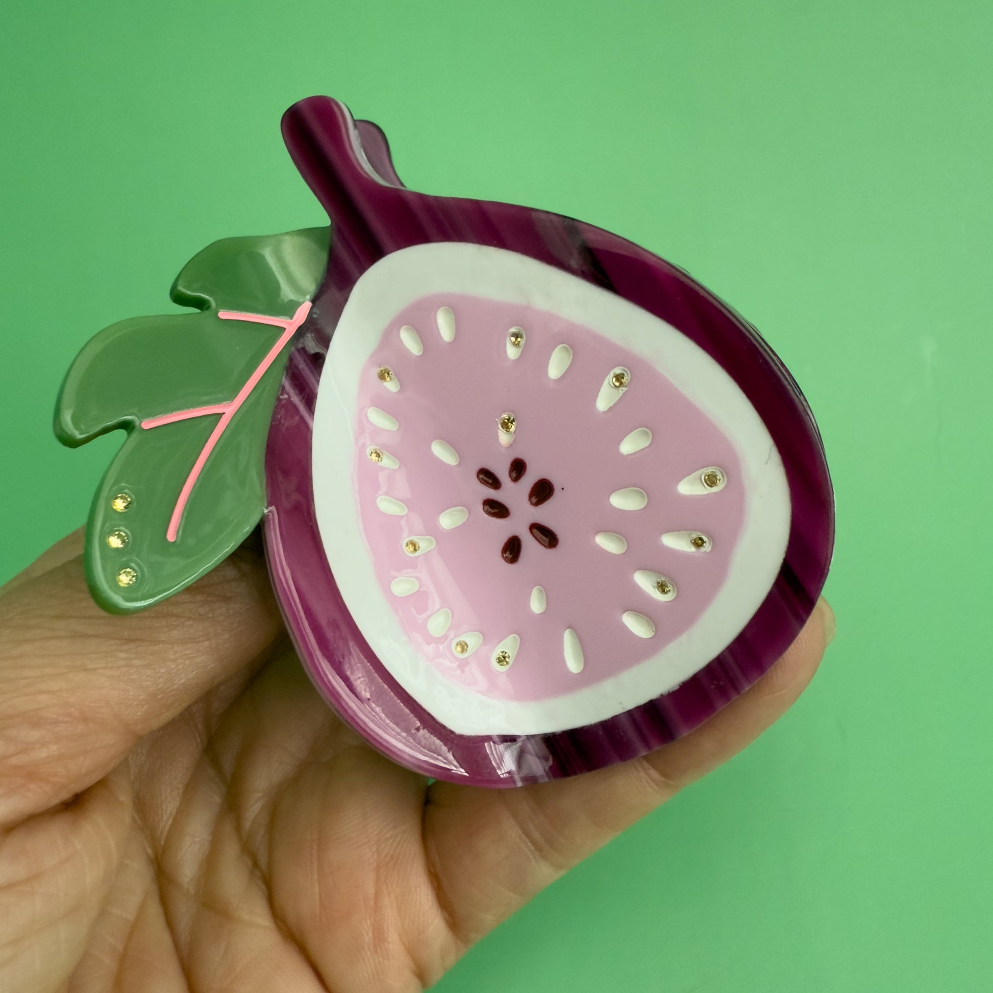 Decorative hair claw like a sliced fig on a green background. 