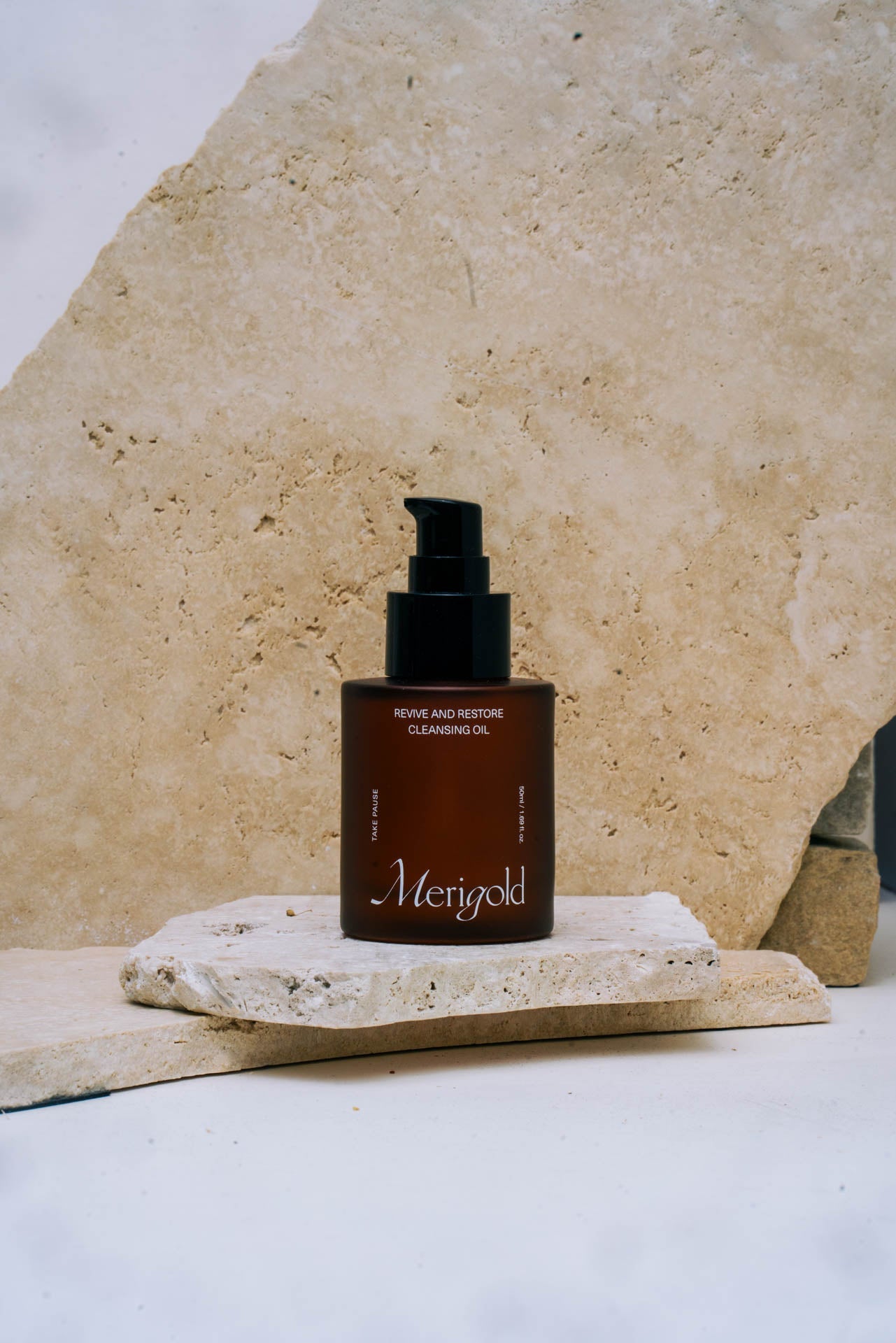 Merigold Revive and Restore Cleansing Oil — natural skincare product in amber glass bottle with pump, photographed on stone background