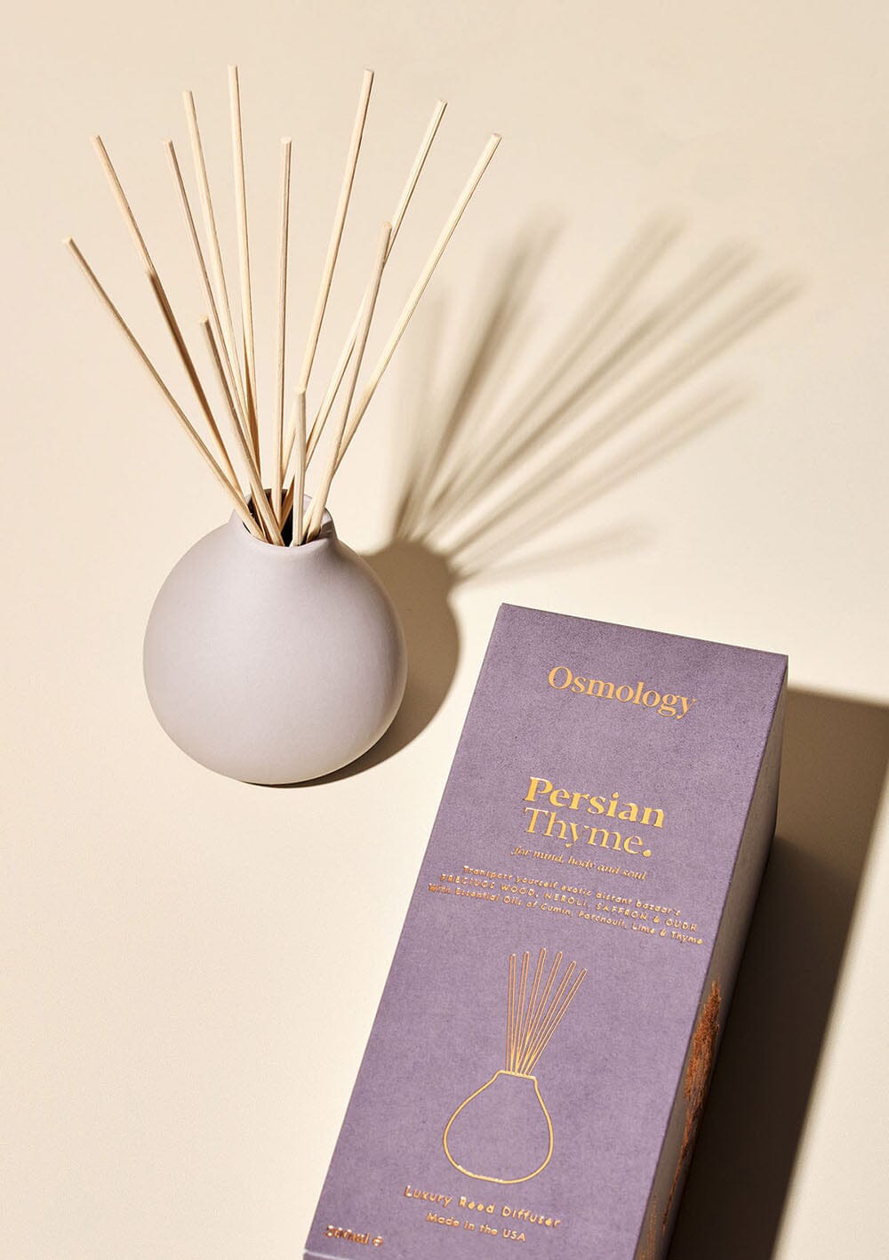 Osmology Persian Thyme grey ceramic reed diffuser next to product packaging on a white background