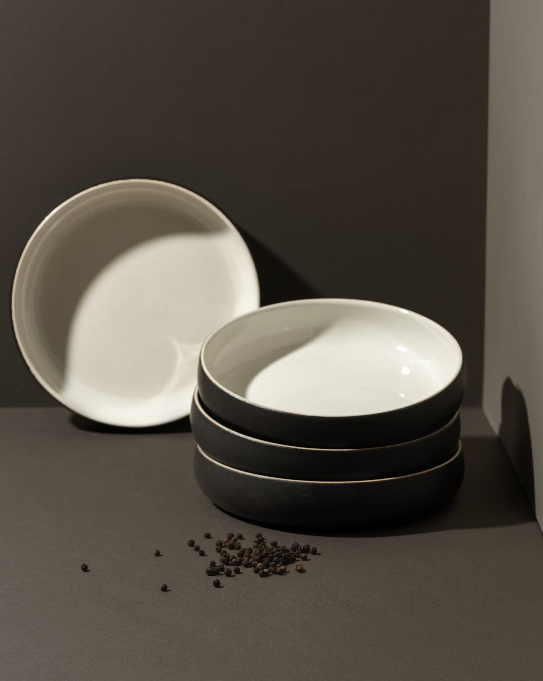 A beige stoneware pasta/salad plate with a contemporary round shape, displayed in a stacked arrangement with a white vegetable on the side.