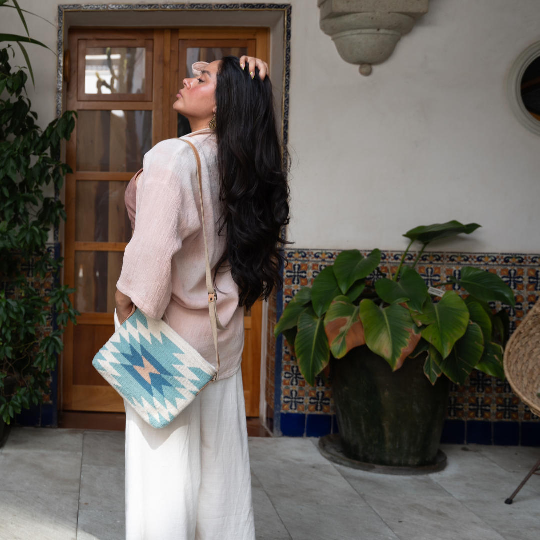 Woman carrying handwoven crossbody bag with abstract Zapotec diamond design in soft spring tones; features adjustable leather strap and two internal pockets for daily essentials
