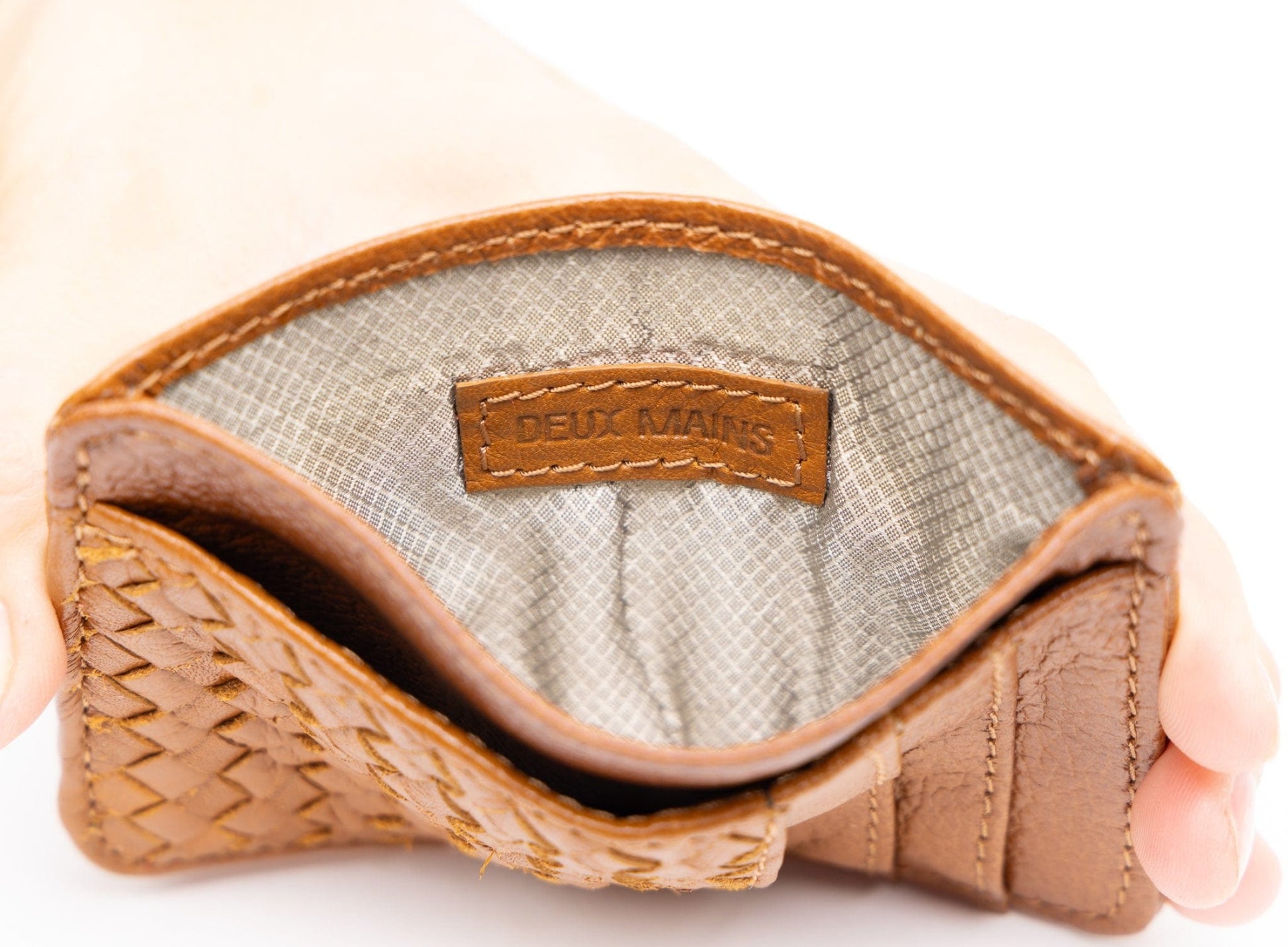 Close-up of a cognac leather product with 'DEUX MAINS' branding on a white background