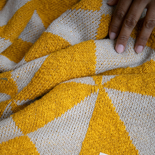 Close-up of a hand touching a knitted throw with bright yellow and white geometric patterns.