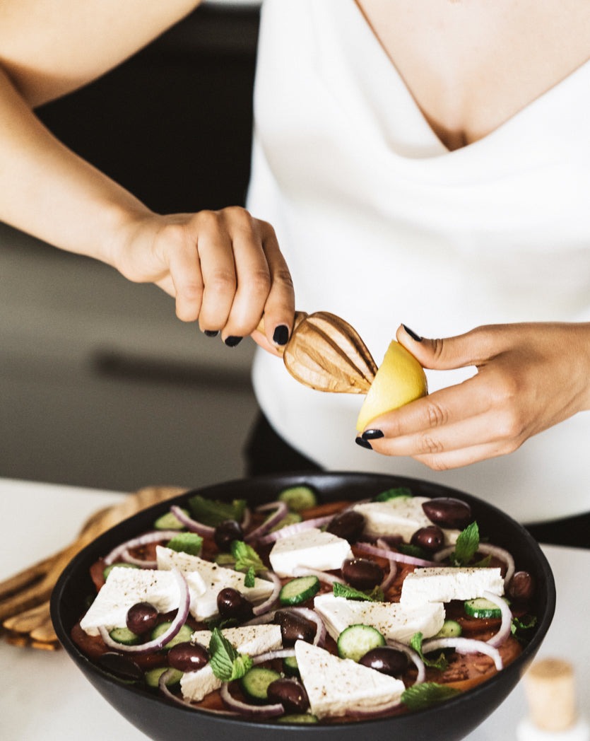 Person using a wooden lemon press to squeeze lemon juice over a bowl of salad on the table