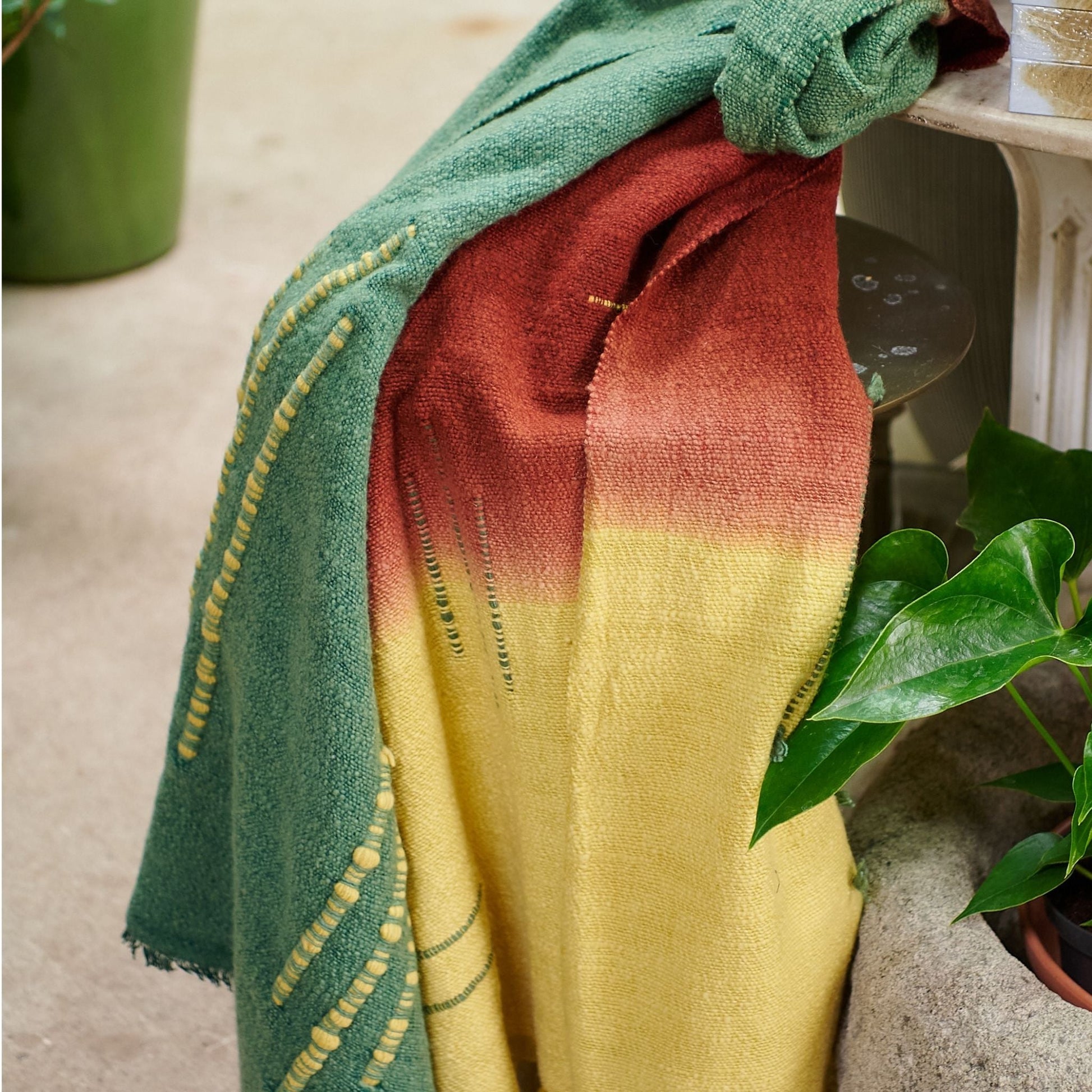 Avocado Green Multi Color Warm Hues Hand Woven Hand Knotted Textured Merino Throw draped over furniture with plants.