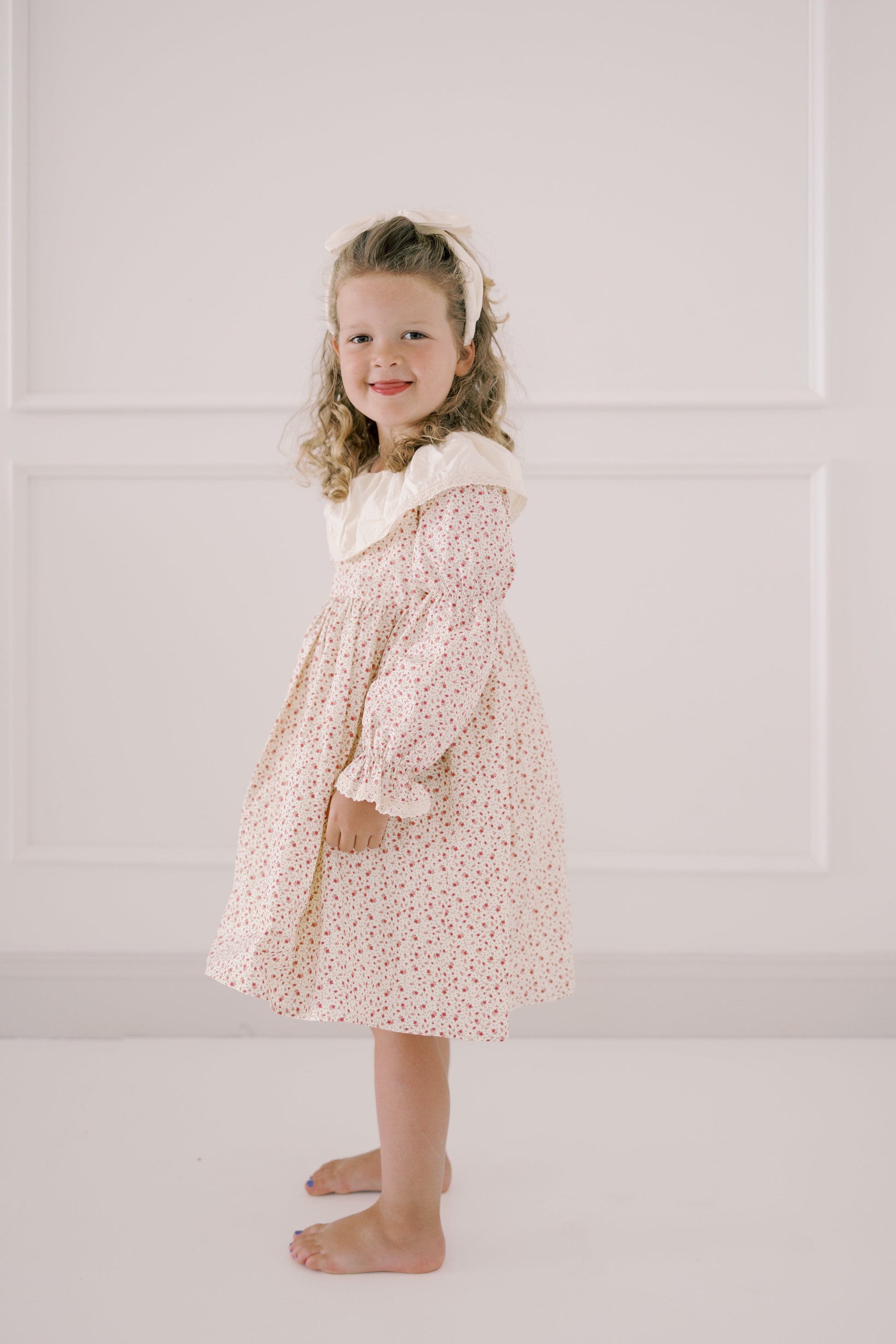 Young girl wearing a floral dress with a white headband against a light background