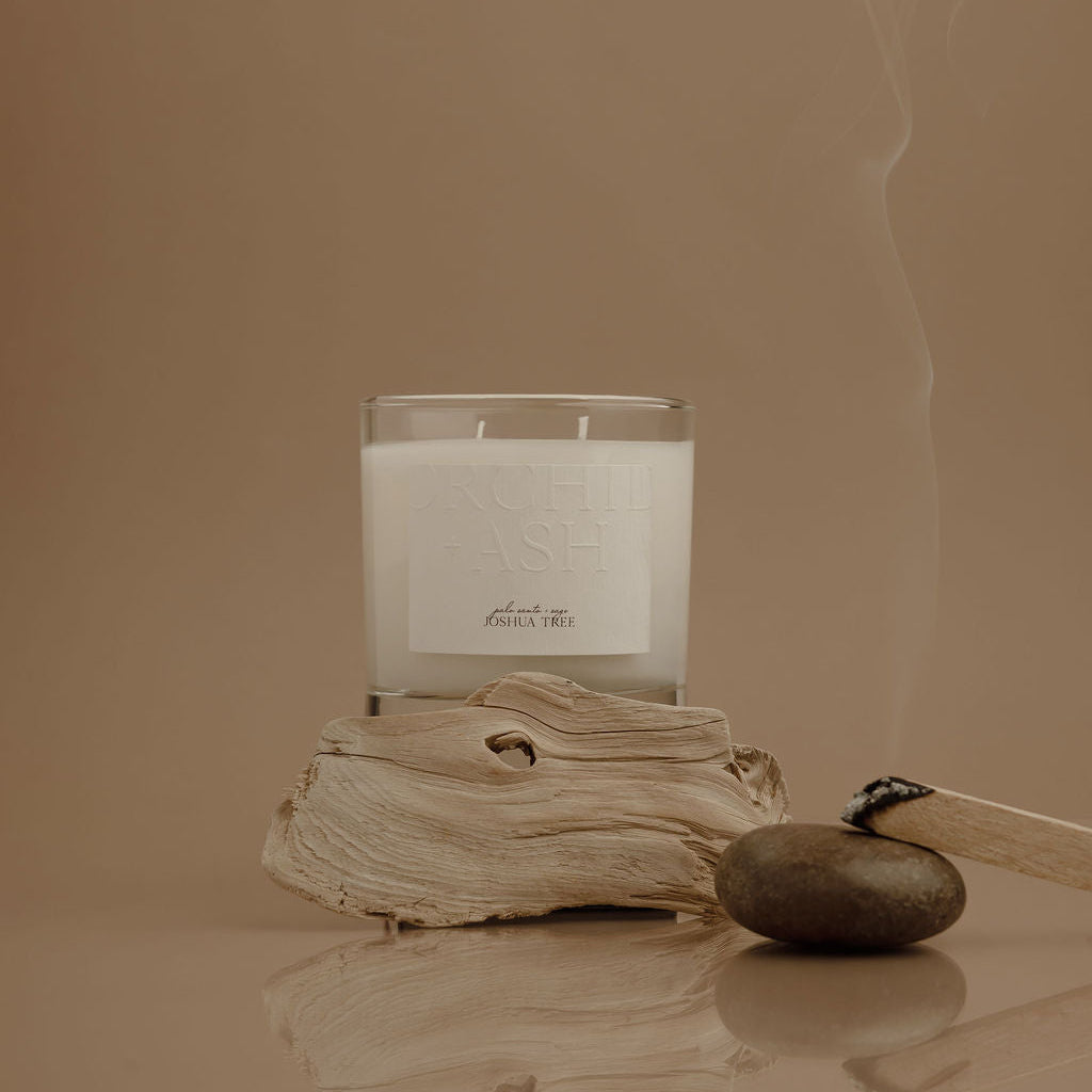 Candle with a label on a piece of driftwood against a beige background