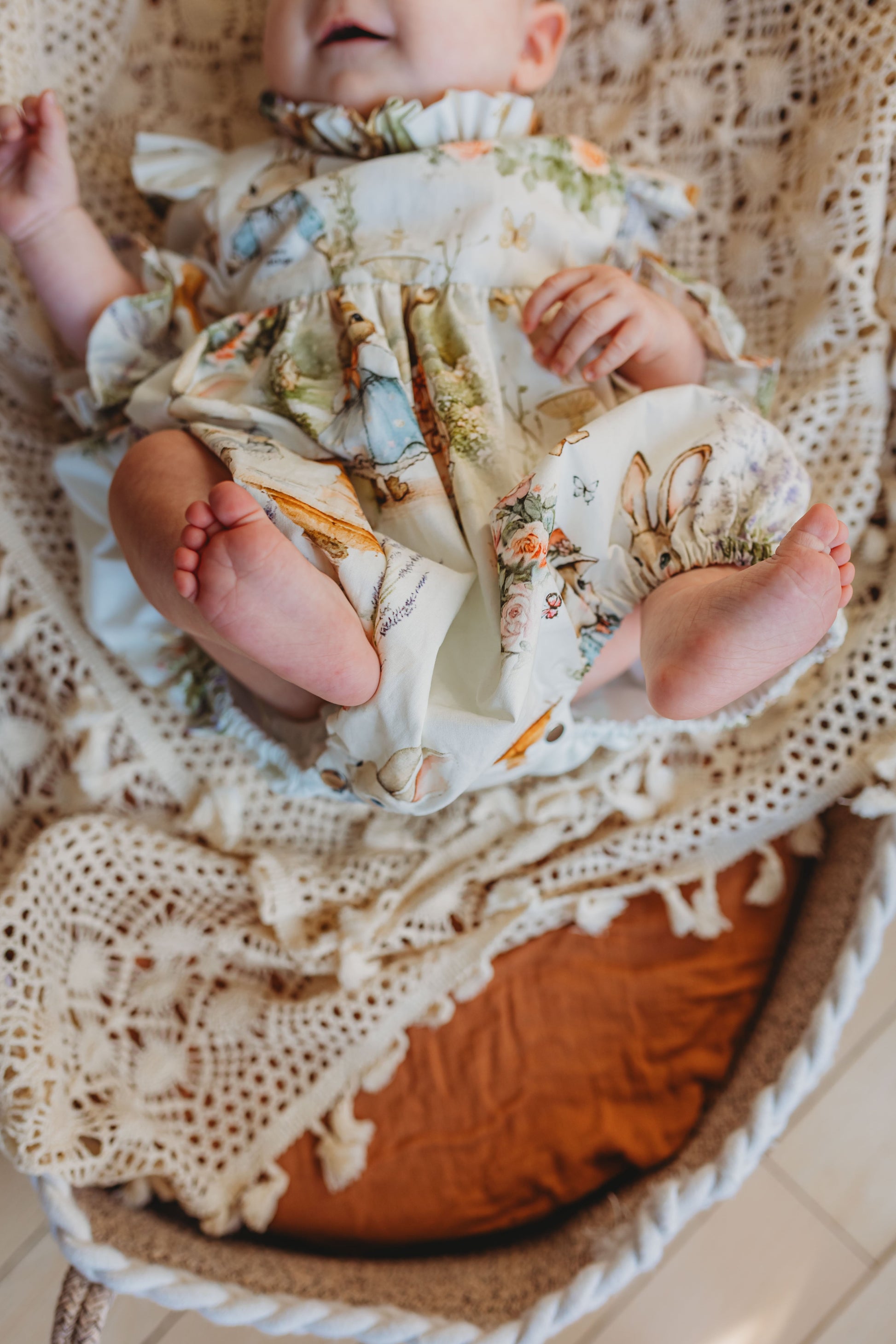 Baby wrapped in a floral blanket with bunny patterns, sitting on a textured surface.