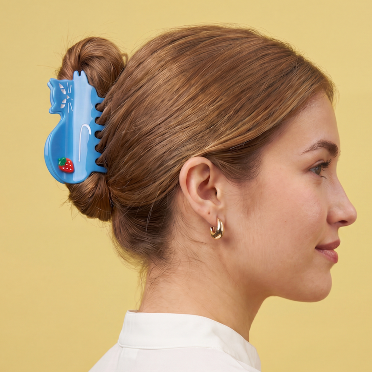 Woman with a bun using a blue cat hair claw clip against a yellow background