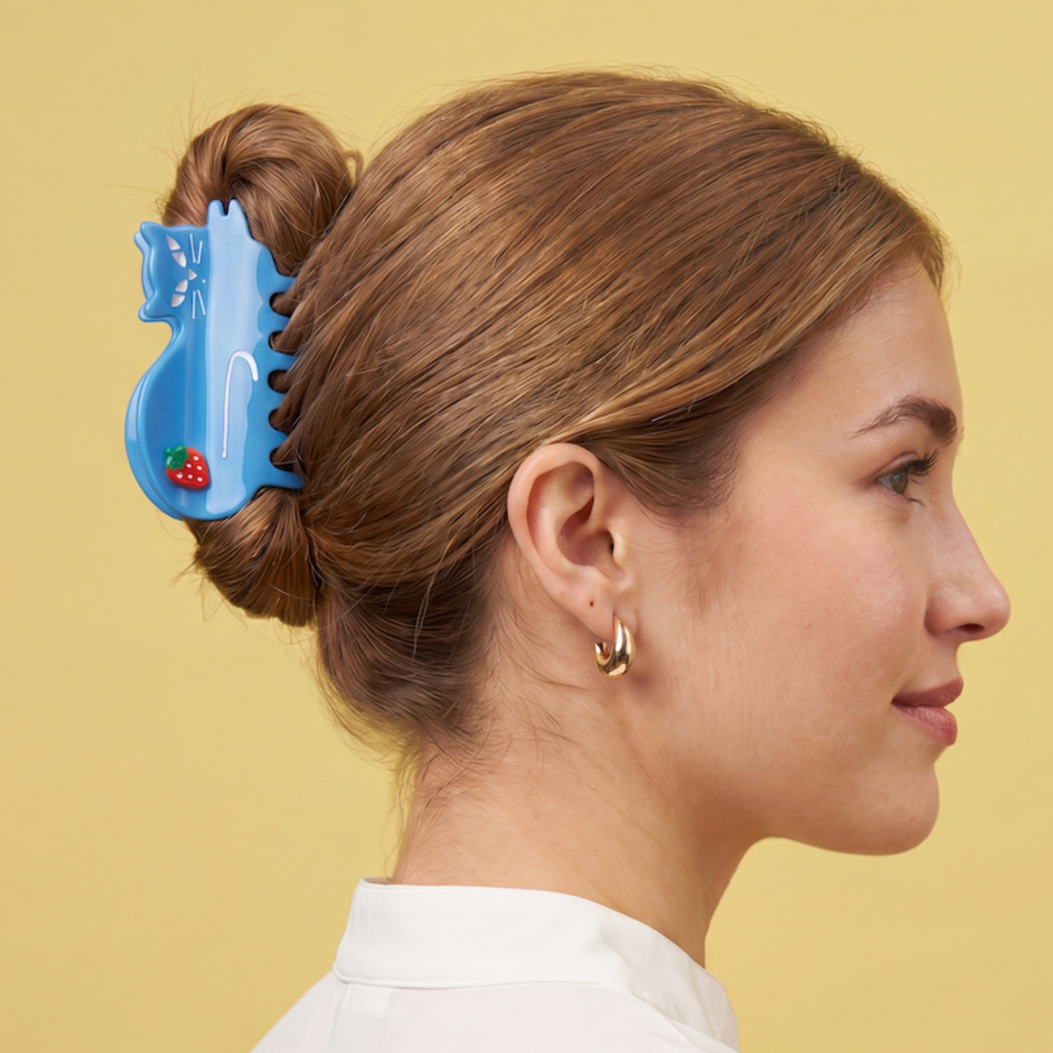 Woman with a bun using a blue cat hair claw clip against a yellow background