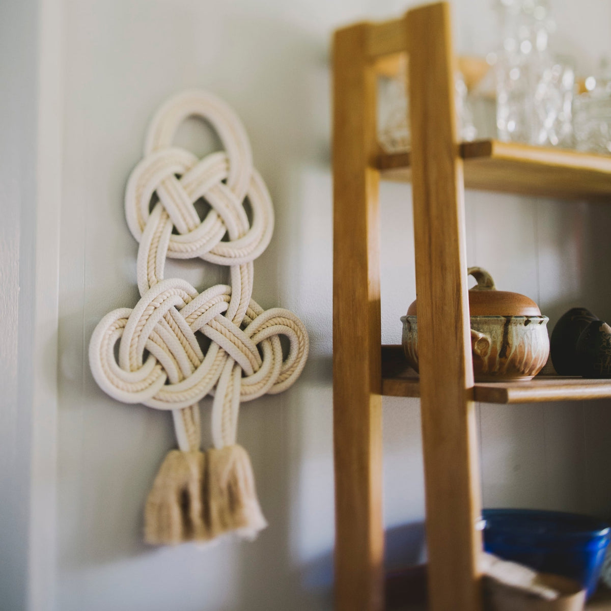 Coexist knotted cream cotton rope wall hanging beside a wooden shelf