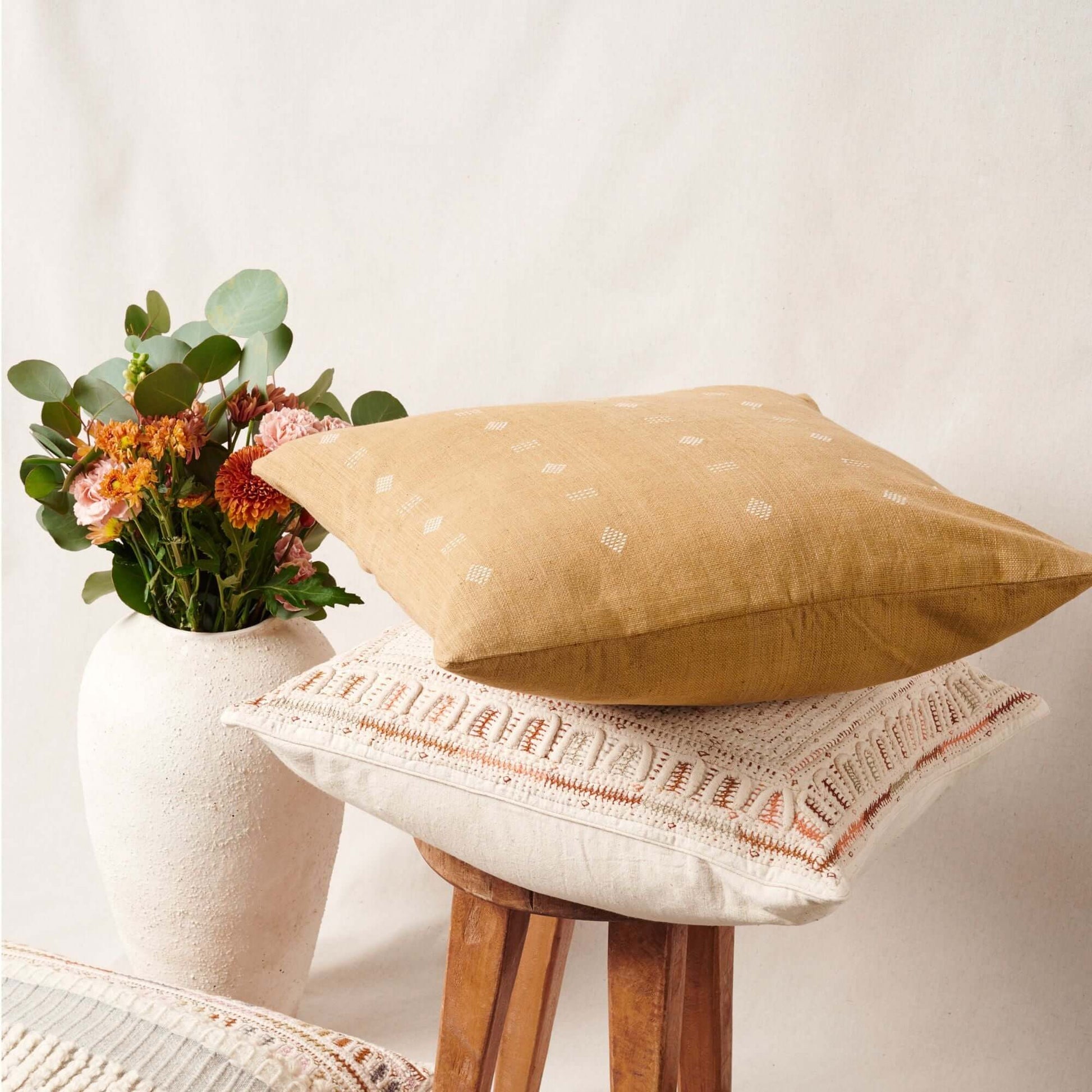 Nira Ochre Hand Spun Organic Cotton Handloom Pillow on a stool beside flowers in a modern vase.
