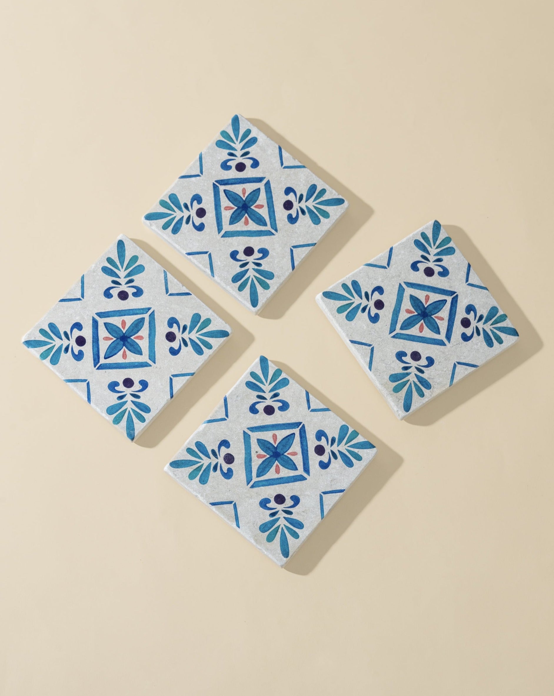 A set of four square white marble coasters with blue floral patterns, arranged on an off-white background, showcasing their elegant and handcrafted design.
