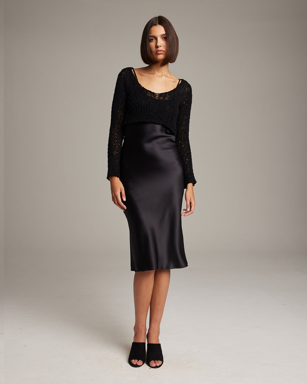 Model wearing a black Flammé Loose Knit Cropped Sweater over a satin dress