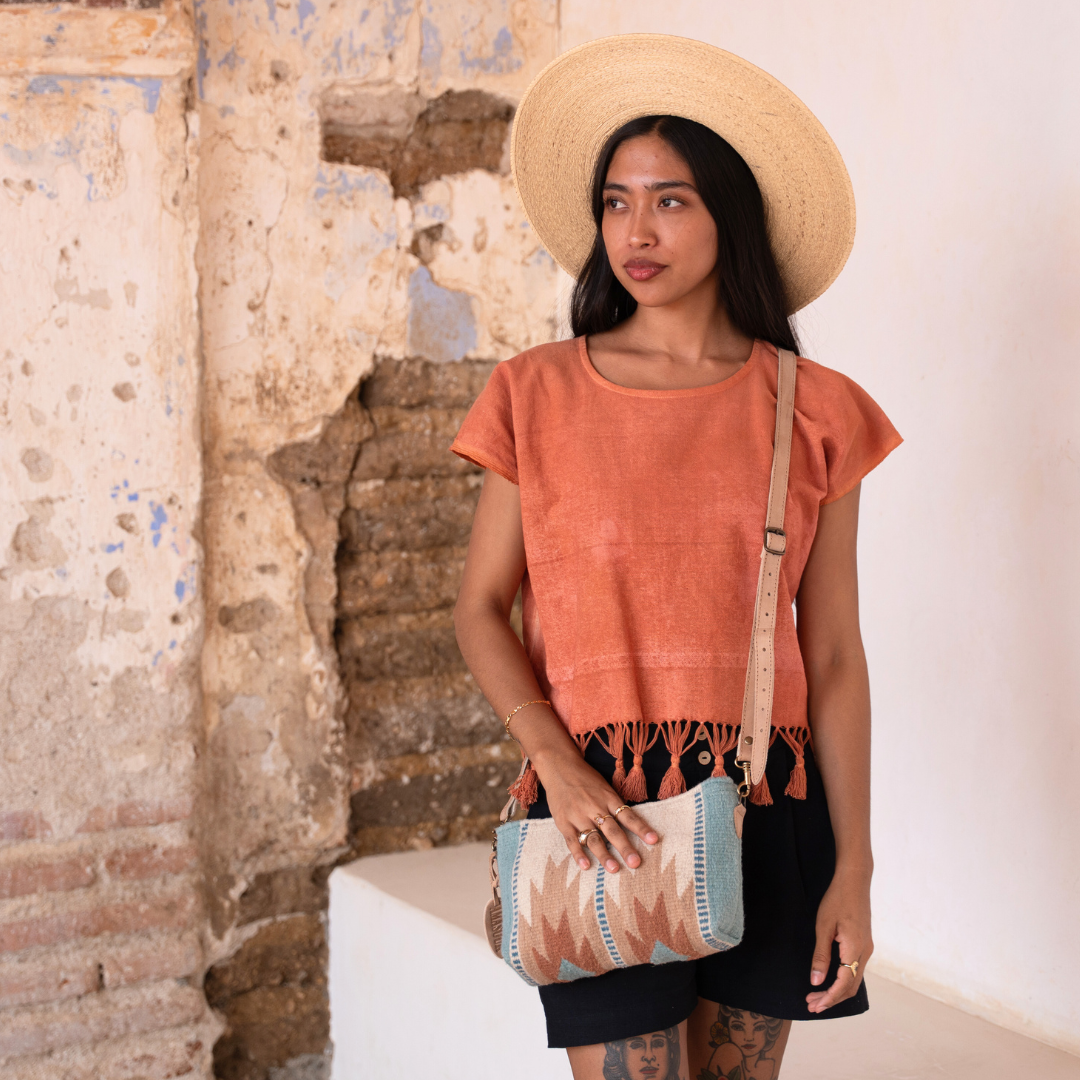 Woman wearing handwoven convertible clutch with Zapotec lightning design in rose and blue tones; functions as a pouch, wristlet, or crossbody with leather straps and internal pocket
